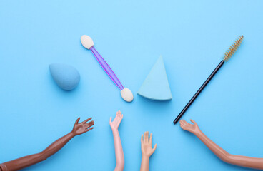 Doll's hands holding makeup accessories on blue background