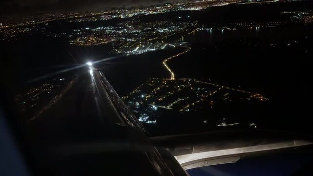 View from cabin of airplane with marker lights flying over night cityscape with river and bridge. Flying passenger plane over modern city in darkness. Business flights between cities. Grain texture