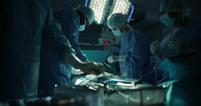 Skilled Male and Female Surgical Team Performing a Delicate Procedure in a Dimly Lit, Technological Hospital Room. Group of Healthcare Professionals Collaborating Around the Operating Table