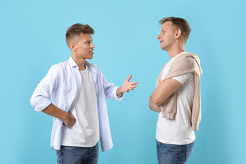 Two young brothers talking on light blue background