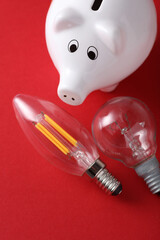 Incandescent and Energy Saving Filament Light Bulbs with piggy bank on red Background. Save money