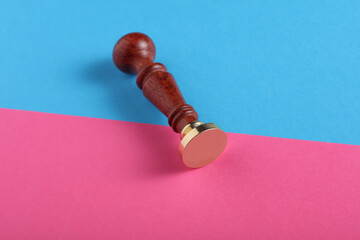 Vintage personal stamp with wooden handle and bronze head on blue pink background. Top view