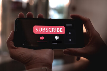 Close-up view of a woman using a smartphone to press red subscribe button on online media. Concepts of technology and following news, hot trends and new content on social media