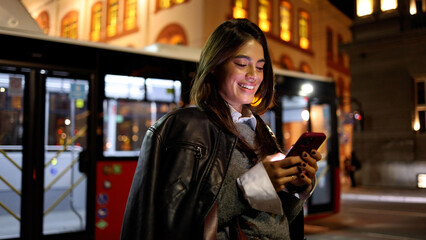 Fototapeta premium Happy woman using phone during a nighttime walk downtown
