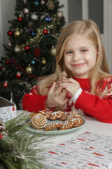 Adorable little girl enjoying winter holidays at home, wearing Christmas sweater, gingerbread cookies on the table, cozy festive atmosphere.	
