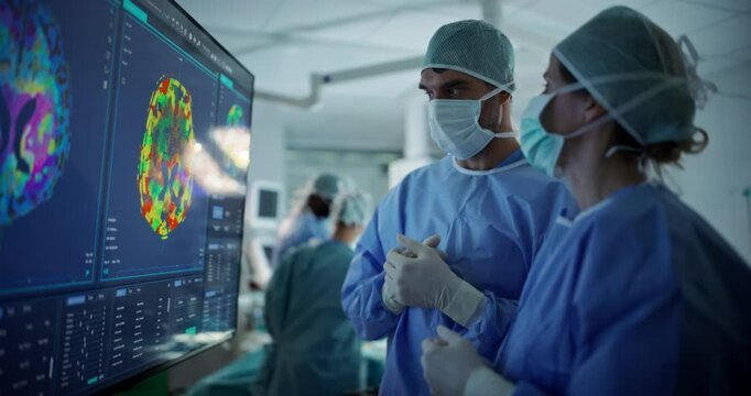Before Beginning the Surgery, Female Lead Surgeon and an Assistant Looking at Detailed Brain PET Scans on a Large Computer Screen, Making Key Decisions Together with the Team