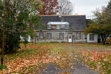 Selective focus view of historic asymmetrical field stone house with steep shingled roof and white...