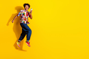 Full size photo of nice young man jump run hold phone wear shirt isolated on bright yellow color background