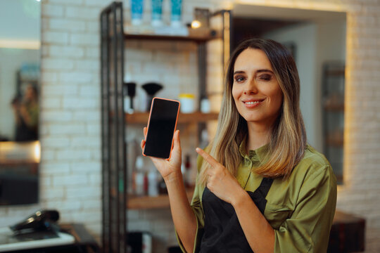 Happy Hairdresser Pointing to her Phone Display for Appointments. Friendly Hair Salon receptionist Ready to Schedule Appointment 
