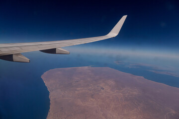 Awesome view of the Earth under the airplane wing. Amazing landscape is visible through airplane window. Traveling by plane. Flying in the sky among clouds.