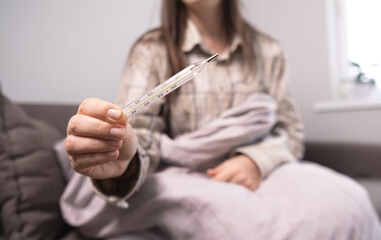 Woman with fever checks her temperature with a thermometer, essential first-aid supplies and home medicine kits nearby.