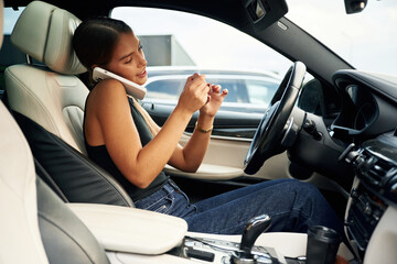 Side view, talking by phone. Woman is sitting in the car