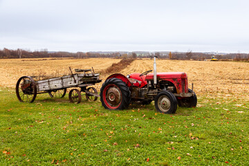 Obraz premium Selective focus view of vintage tractor with wooden trailer set as decoration in field during a grey fall morning, Saint-Michel-de-Bellechasse, Quebec, Canada