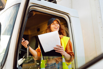 Young woman professional truck driver checking shipment list on a -parking lot. Transport industry theme.