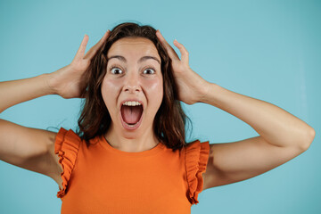 Portrait of young woman on blue background. Face of surprise and fear. With her hands placed on her head on both sides. Woman isolated.