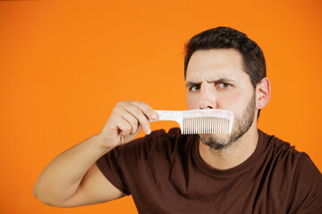 Portrait of a young man combing his bangs with a comb or brush. Male beauty, grooming his hair. Portrait made on an orange background.