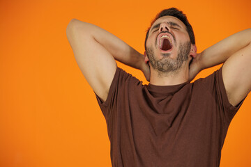 Young handsome guy isolated over orange background. He is very tired, he keeps yawning. He shows...