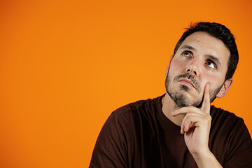 Portrait of young man thinking looking up and with his hand resting on his chin. Isolated over...