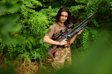 A soldier in camouflage stands confidently in a lush green forest holding a rifle, showcasing bravery and focus in a military training environment