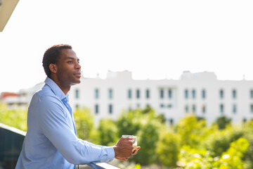 Man holding a coffee cup while looking out from a balcony