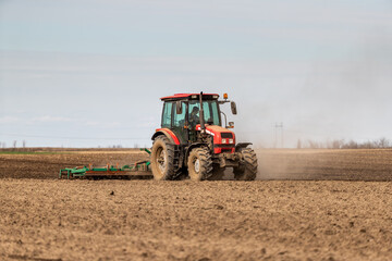 Obraz premium Farmer works the land, plowing a field with a modern red tractor on a sunny day