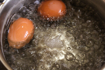 two brown chicken eggs are boiled in a saucepan