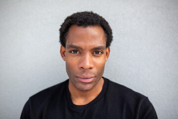 Close-up portrait of a man with a neutral expression against a grey wall