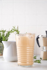 Glass of iced scented aromatic rosemary coffee latte, with whipped milk or cream, cold coffee drink decorated with sprig of rosemary