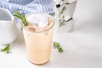 Glass of iced scented aromatic rosemary coffee latte, with whipped milk or cream, cold coffee drink decorated with sprig of rosemary