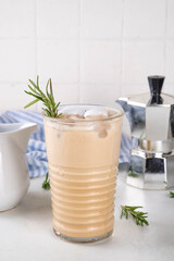 Glass of iced scented aromatic rosemary coffee latte, with whipped milk or cream, cold coffee drink decorated with sprig of rosemary