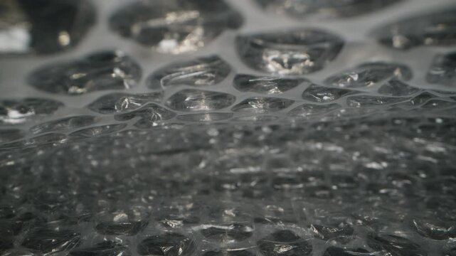 Dolly slider close-up of bubble wrap surface, emphasizing the inflated air pockets and glossy, transparent texture, showing intricate detail in a shallow depth of field.