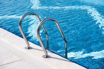 A Stainless still ladder for descending into the pool. Modern swimming pool with ladder at resort