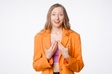 surprised young woman in confusion pointing at herself. Concept of bewilderment, astonishment, self-doubt, and disbelief. Female posing on a white studio background, wearing an orange blazer