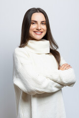 Portrait of a gorgeous woman wearing a white sweater, on light gray background.