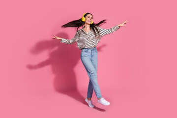 Joyful young woman dancing with headphones against pink background in casual style