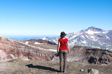 one girl tourist climbs volcano in Kamchatka, stands with back in red t-shirt against natural volcanic landscape, adventure and travel concept