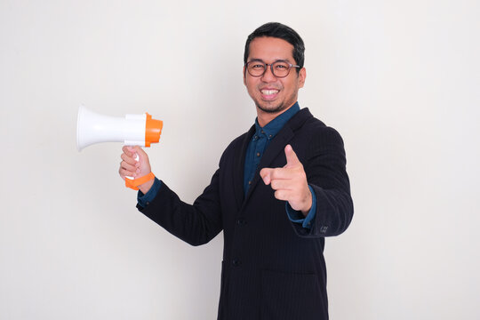 A man wearing suit smiling happy while pointing at the camera and holding megaphone