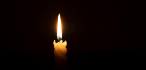 A single burning candle flame or light glowing on a spiral white candle on black or dark background...