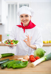 Female chef in white uniform showing approving gesture satisfied with vegetable salad