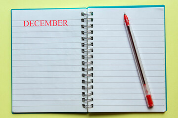 the word DECEMBER written on an open notepad, with a red pen next to , on yellow background