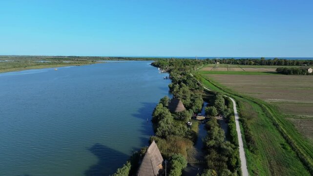 shoreline aerial flight on the Nicesolo canal over the Casoni di Caorle traditional fishing village architecture and modern-day fishing grounds for commercial fishing