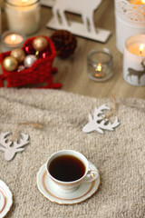Various Christmas decorations, lit candles, cup of tea or coffee, cookies, books, presents and soft blanket on the table. Holiday hygge at home. Selective focus.