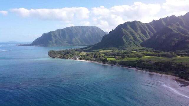 Cinematic aerial view dramatic mountains blue ocean at Kualoa Ranch park, Punaluu beach park. Coast of Oahu island Hawaii USA. Beautiful nature view of green jungle mountain peaks with tropical beach