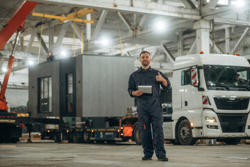 Part of the house is transported by a truck. Male worker is in the modern warehouse or manufacturing company