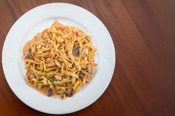 Delicious tagliatelle pasta in creamy tomato sauce with shrimp and mushrooms, garnished with herbs, served on a white plate.

