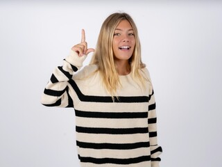 caucasian teen girl wearing striped knitted sweater over white pointing finger up and looking inspired by genius thought, showing good idea sign, having clever solution in mind