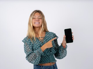 Smiling caucasian teen girl wearing green dress over white Mock up copy space. Pointing index finger on mobile phone with blank empty screen