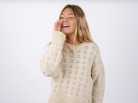 caucasian teen girl wearing knitted sweater over white look empty space holding hand face and screaming or calling someone.