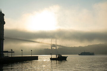 Fototapeta premium Pigeons flying over the Bosphorus on a foggy morning. The 15 July Martyrs Bridge and Ortaköy Mosque in a fog. 
