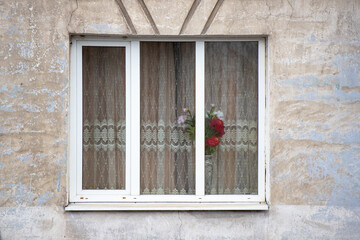 A window with a white curtain and a vase of flowers in it